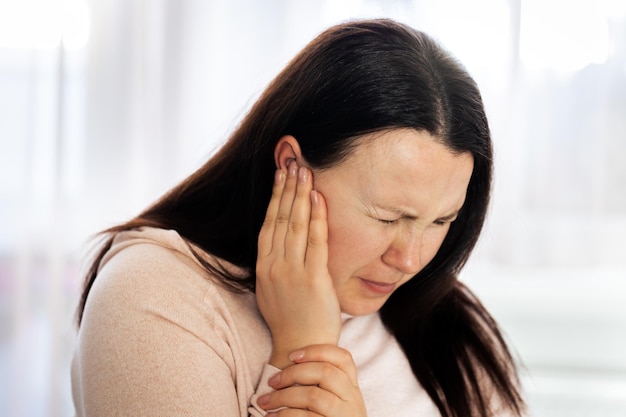 Giovane donna che soffre di forte dolore all'orecchio e acufene dopo il concetto di assistenza sanitaria per la malattia dell'orecchio covid