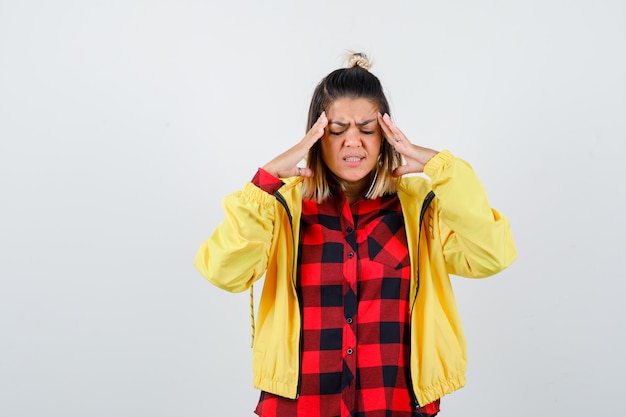 Giovane donna che soffre di mal di testa in camicia a scacchi, giacca e sembra dolorosa. vista frontale.