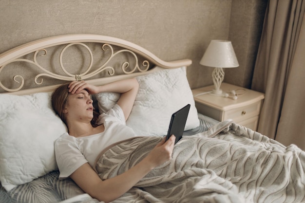 Giovane donna che soffre di mal di testa influenza malato malato freddo a casa coperta sdraiata sul letto con tablet digitale