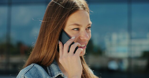 Giovane donna che sorride fiducioso parlando sullo smartphone in strada Ritratto femminile volto ragazza che ha conversazione utilizza lo smartphone in strada moderna