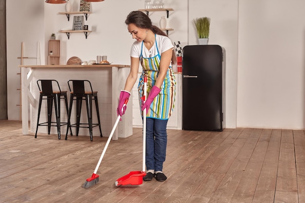 Giovane donna che spazza il pavimento in cucina