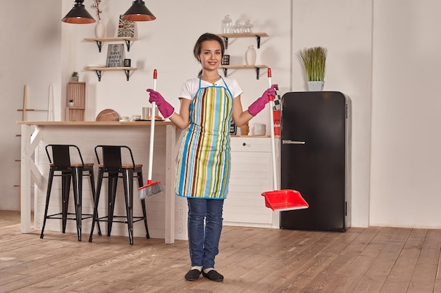 Giovane donna che spazza il pavimento in cucina