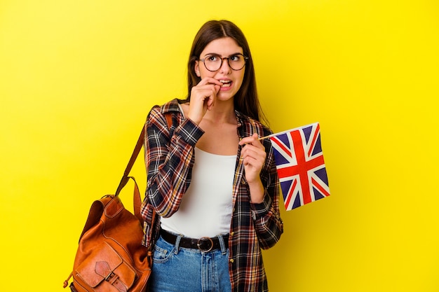 Giovane donna che studia inglese isolata su sfondo rosa che si morde le unghie, nervosa e molto ansiosa.