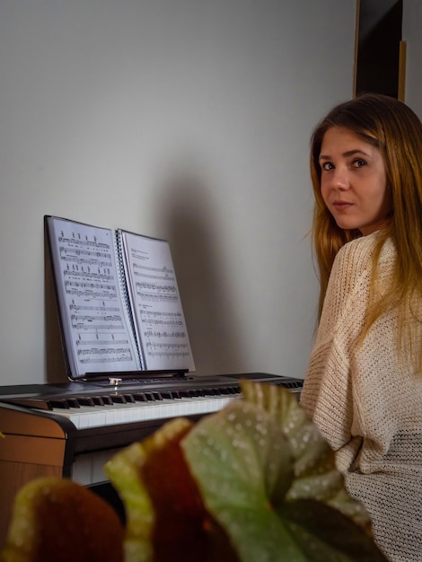 Giovane donna che suona il pianoforte in casa con uno spartito sullo sfondo