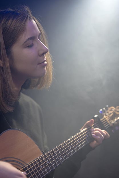 Giovane donna che suona la chitarra acustica in una stanza buia con foschia