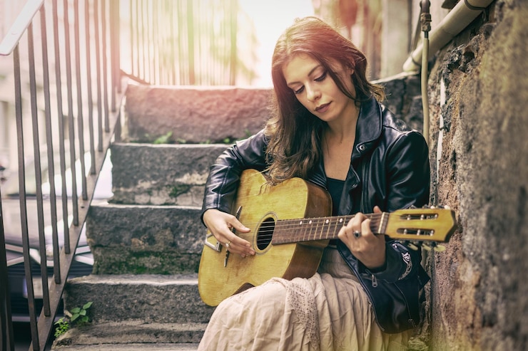 Foto giovane donna che suona la chitarra mentre è seduta all'aperto