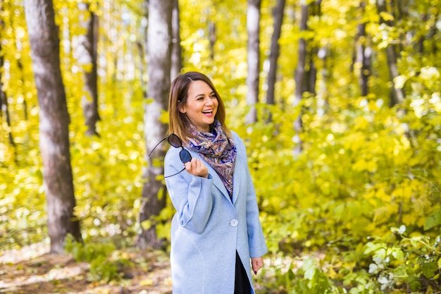 Giovane donna che tiene gli occhiali da sole al parco d'autunno