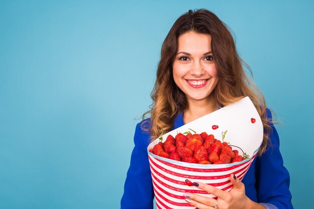 Giovane donna che tiene il mazzo di fragole su sfondo blu