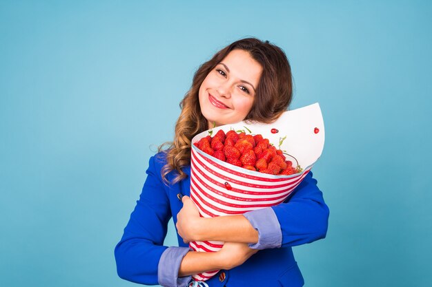 Giovane donna che tiene il mazzo di fragole su sfondo blu