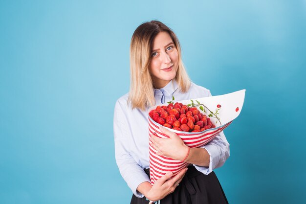 Giovane donna che tiene il mazzo di fragole su sfondo blu