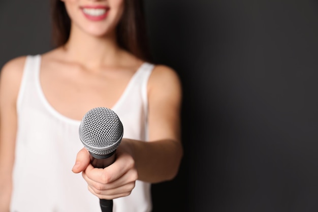 Giovane donna che tiene il microfono su sfondo scuro vista in primo piano con spazio per il testo