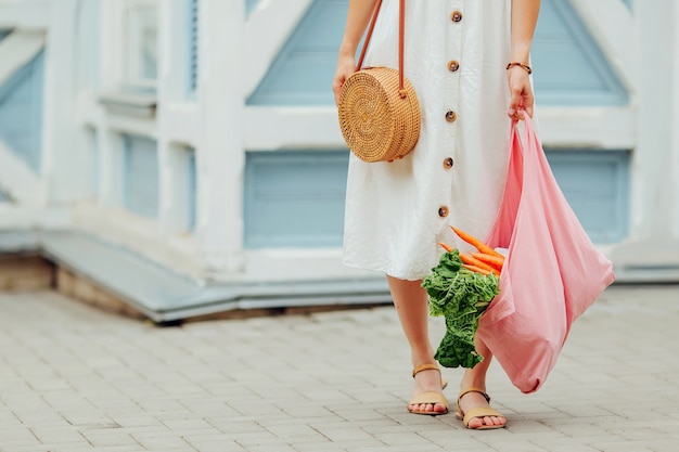 Giovane donna che tiene il sacchetto della spesa in cotone rosa con verdure. Borsa ecologica riutilizzabile per lo shopping. Rifiuti zero concetto.