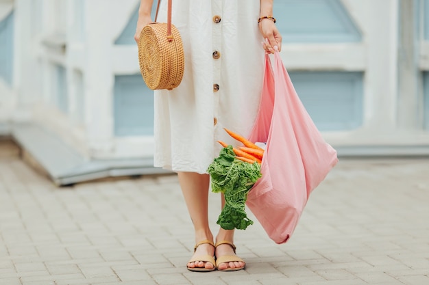 Giovane donna che tiene il sacchetto della spesa in cotone rosa con verdure. Borsa ecologica riutilizzabile per lo shopping. Rifiuti zero concetto.