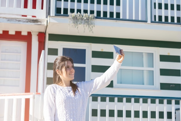 Giovane donna che tiene il suo cellulare per scattare foto con le case colorate di Costa Nova Portogallo
