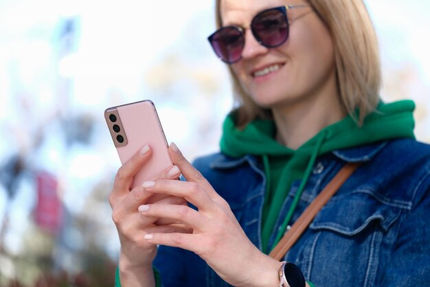 Giovane donna che tiene il telefono cellulare rosa nel parco e la comunicazione sorridente del primo piano nel sociale