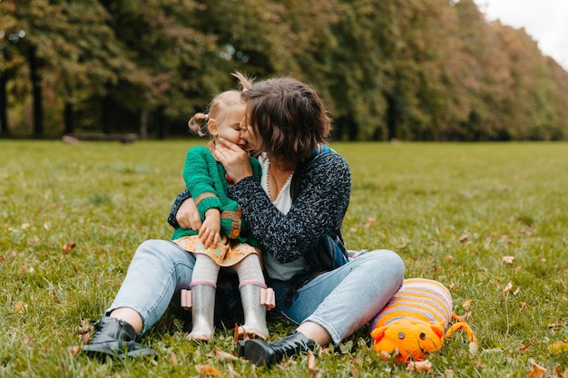 Giovane donna che tiene in braccio un bambino, seduta sull'erba del parco. mamma e figlia stanno camminando nel parco.