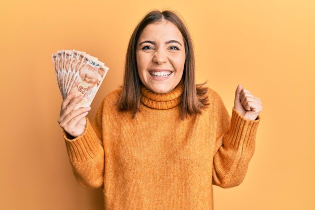 Giovane donna che tiene in mano 50 banconote in lire turche che gridano orgogliose celebrando la vittoria e il successo molto eccitate con il braccio alzato