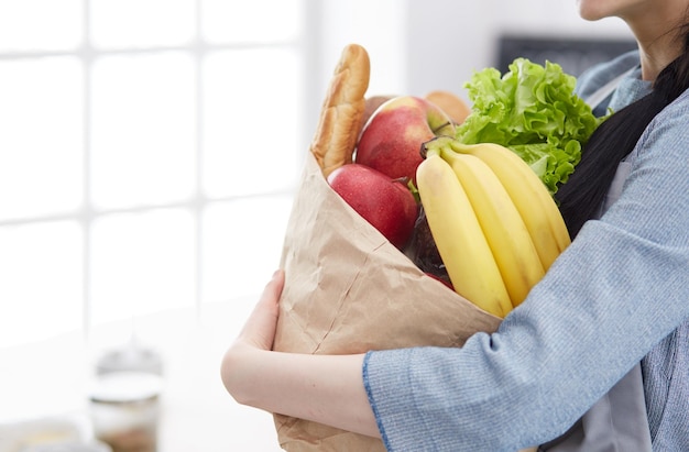 Giovane donna che tiene la borsa della spesa con verdure in piedi in cucina