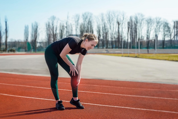 Giovane donna che tiene la gamba dolorante allo stadio. Corsa da trauma sportivo frattura dell'articolazione lussata. Una donna sportiva si tocca la gamba a causa di una distorsione.