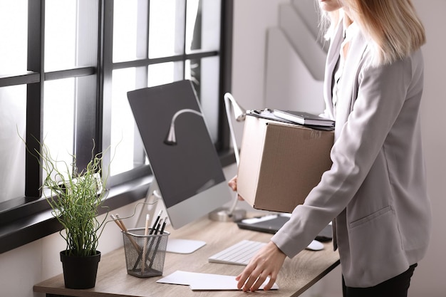 Giovane donna che tiene la scatola commovente con roba dell'ufficio all'interno del primo piano