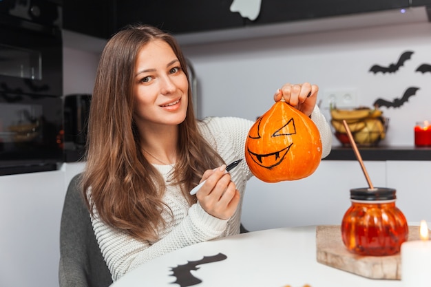 Giovane donna che tiene la zucca per halloween e guarda la telecamera