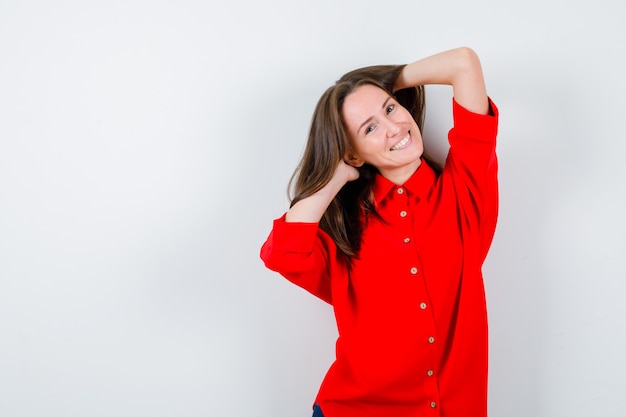 Giovane donna che tiene le mani nei capelli in camicetta rossa e sembra felice, vista frontale.