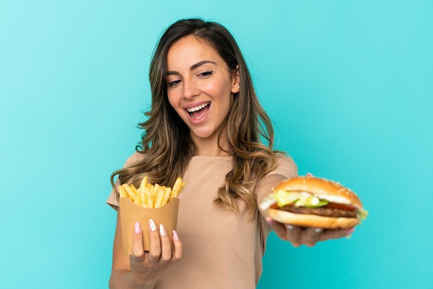 Giovane donna che tiene patatine fritte e hamburger su sfondo isolato