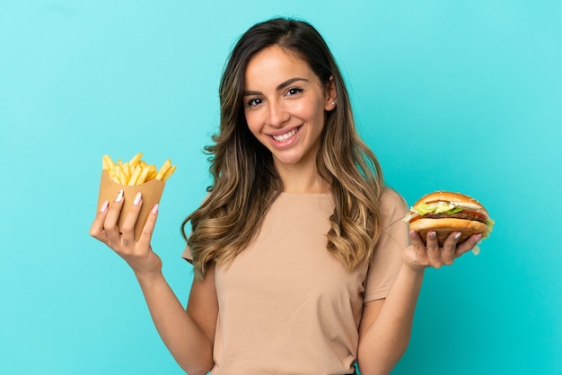 Giovane donna che tiene patatine fritte e hamburger su sfondo isolato
