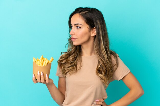 Giovane donna che tiene patatine fritte su sfondo isolato guardando al lato