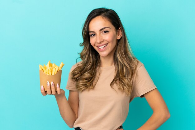 Giovane donna che tiene patatine fritte su sfondo isolato in posa con le braccia all'anca e sorridente