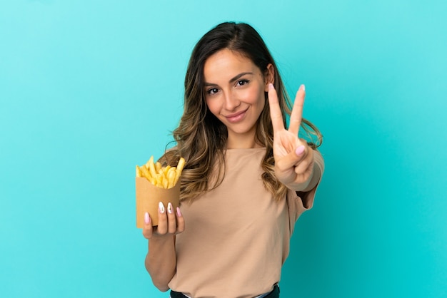 Giovane donna che tiene patatine fritte su sfondo isolato sorridendo e mostrando segno di vittoria victory