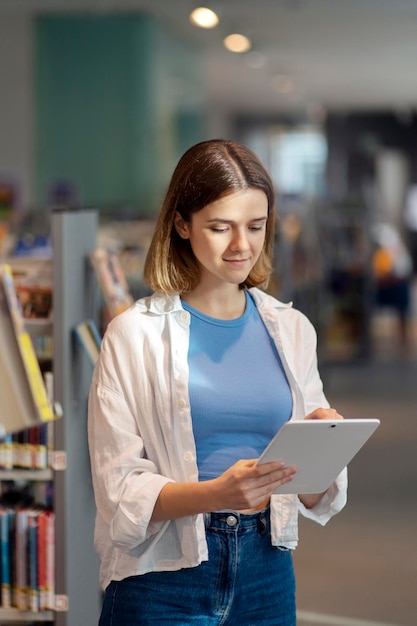 Giovane donna che tiene tavoletta digitale in piedi nel negozio di libri alla ricerca online