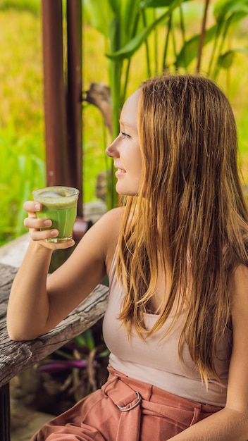 Giovane donna che tiene tazza di tè verde matcha latte sul vecchio formato verticale della tavola di legno del fondo per