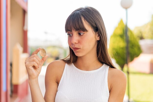 Giovane donna che tiene un Bitcoin all'aperto con espressione triste