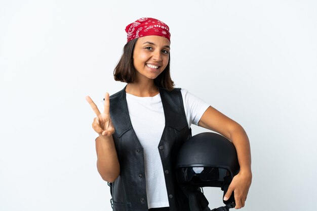 Giovane donna che tiene un casco del motociclo isolato su bianco che sorride e che mostra il segno di vittoria