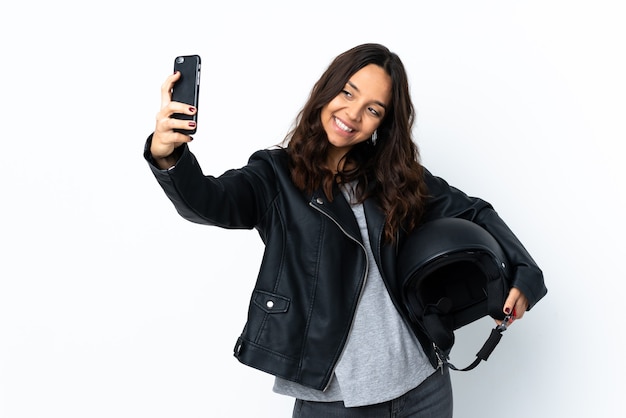 Giovane donna che tiene un casco del motociclo sopra la parete bianca isolata che fa un selfie