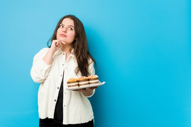 Giovane donna che tiene un cupcakes guardando lateralmente con espressione dubbiosa e scettica.