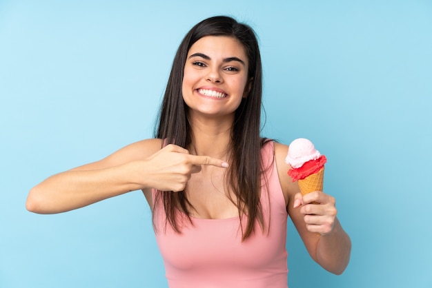 Giovane donna che tiene un gelato alla cornetta sopra il blu isolato e indicandolo