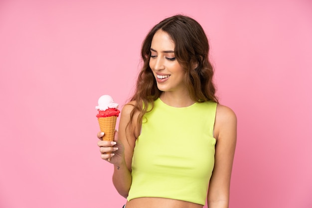 Giovane donna che tiene un gelato della cornetta sopra su una parete rosa con l'espressione felice