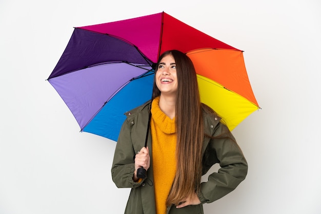 Giovane donna che tiene un ombrello isolato su sfondo bianco in posa con le braccia all'anca e sorridente