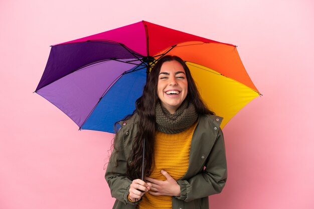 Giovane donna che tiene un ombrello isolato su sfondo rosa sorridente molto