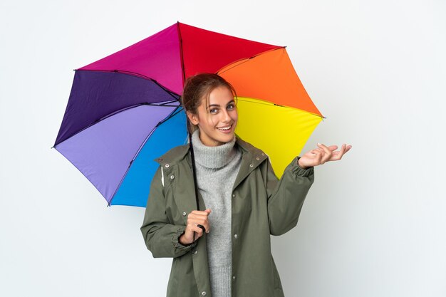 Giovane donna che tiene un ombrello su priorità bassa bianca che estende le mani a lato per invitare a venire