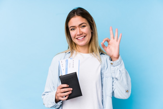 Giovane donna che tiene un passaporto allegro e sicuro che mostra gesto giusto