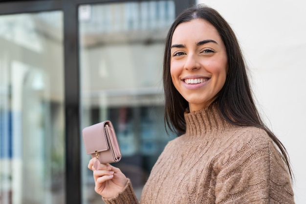 Giovane donna che tiene un portafoglio all'aperto che sorride molto