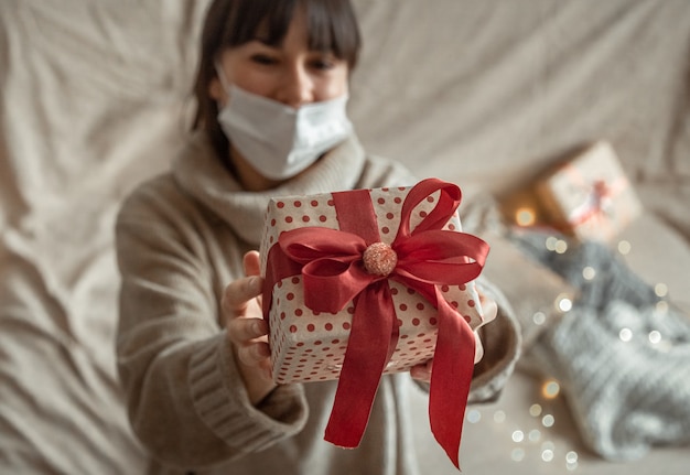 Giovane donna che tiene un regalo di Natale splendidamente avvolto. Concetto di celebrare il Natale durante la pandemia di coronavirus.