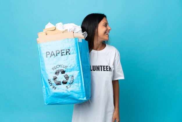 Giovane donna che tiene un sacchetto di riciclaggio pieno di carta che ride in posizione laterale