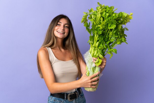 Giovane donna che tiene un sedano isolato su viola con felice espressione