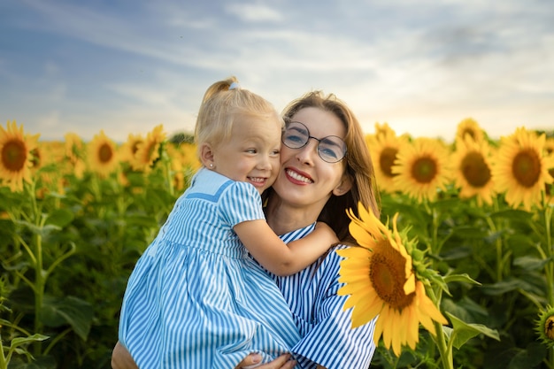 Giovane donna che tiene una bambina in braccio su un campo di girasoli.