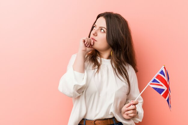 Giovane donna che tiene una bandiera del Regno Unito che guarda lateralmente con espressione dubbiosa e scettica.