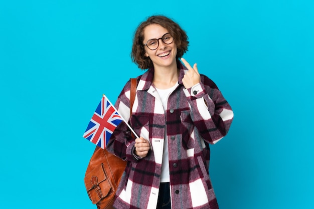 Giovane donna che tiene una bandiera del Regno Unito in posa isolata contro il muro bianco
